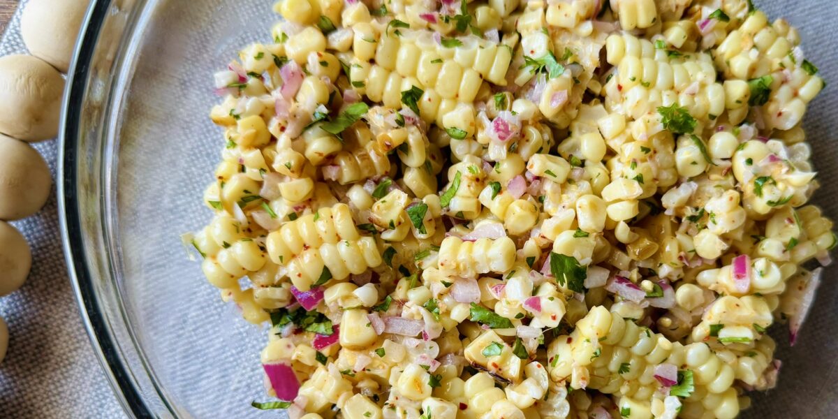 a clear glass bowl with creamy roasted corn salad on a table