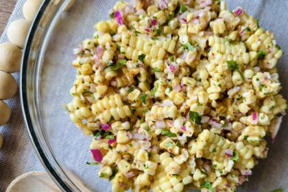 a clear glass bowl with creamy roasted corn salad on a table