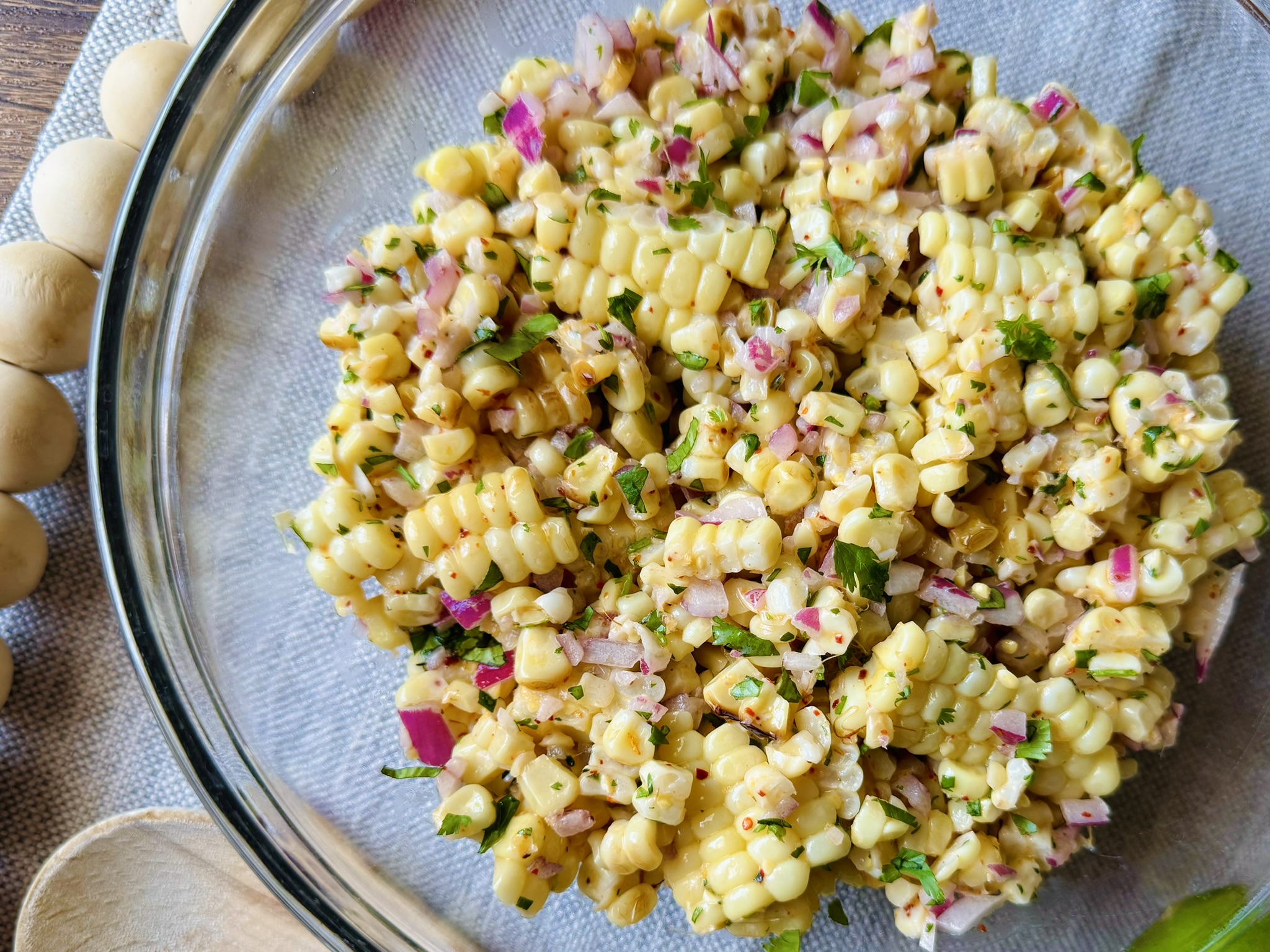 a clear glass bowl with creamy roasted corn salad on a table