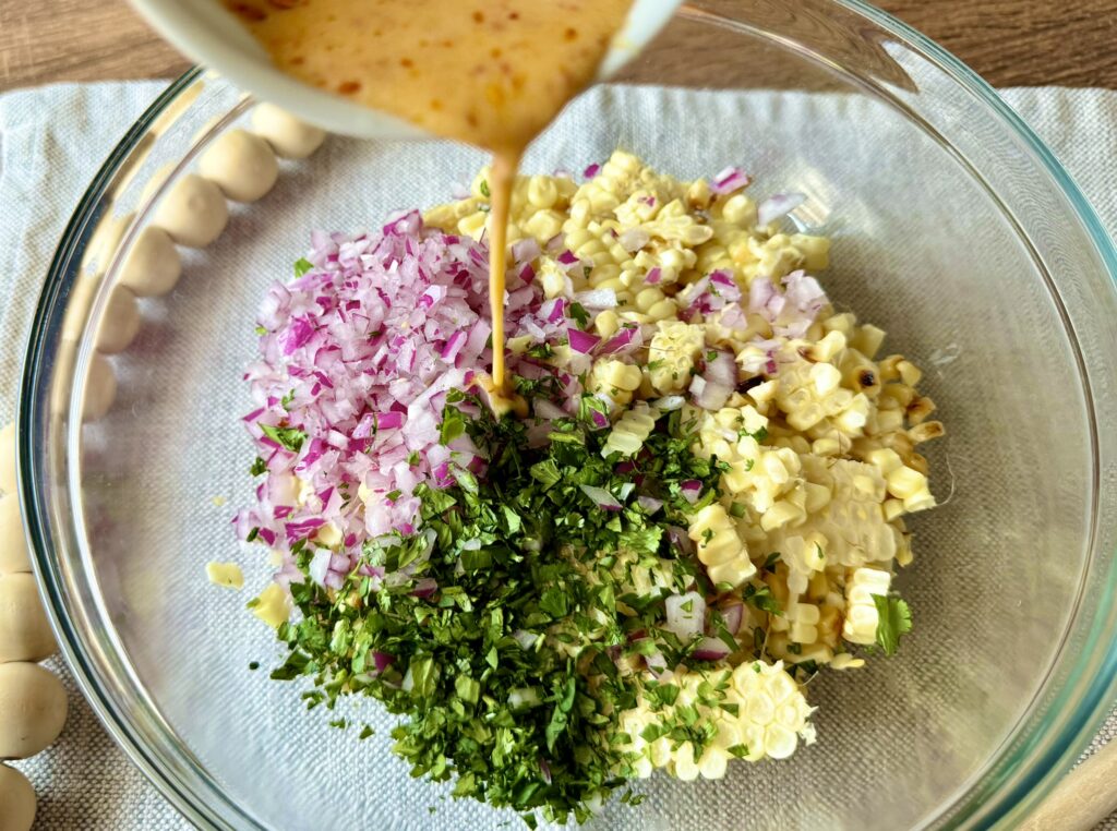 lime dressing being poured over a corn salad in a clear bowl