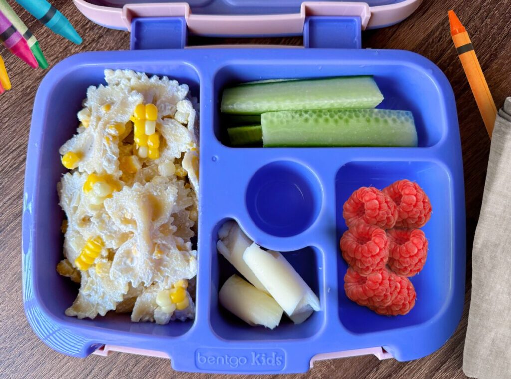 kids bento lunch box with pasta salad, string cheese and cucumber slices