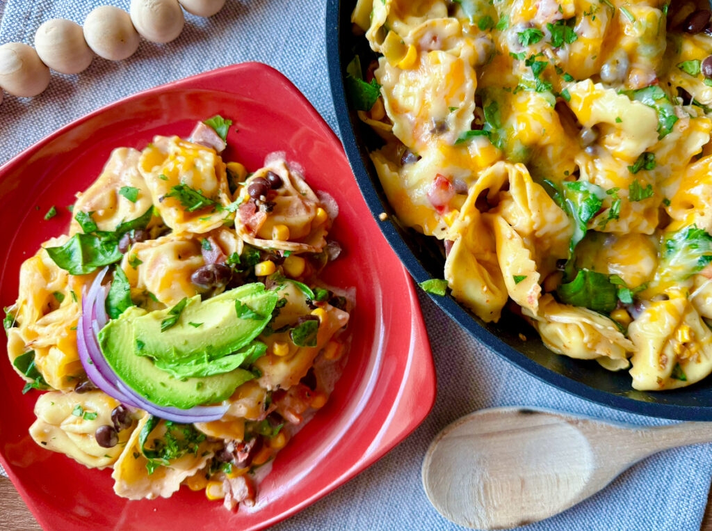 red plate with cheesy tortellini on top next to skillet