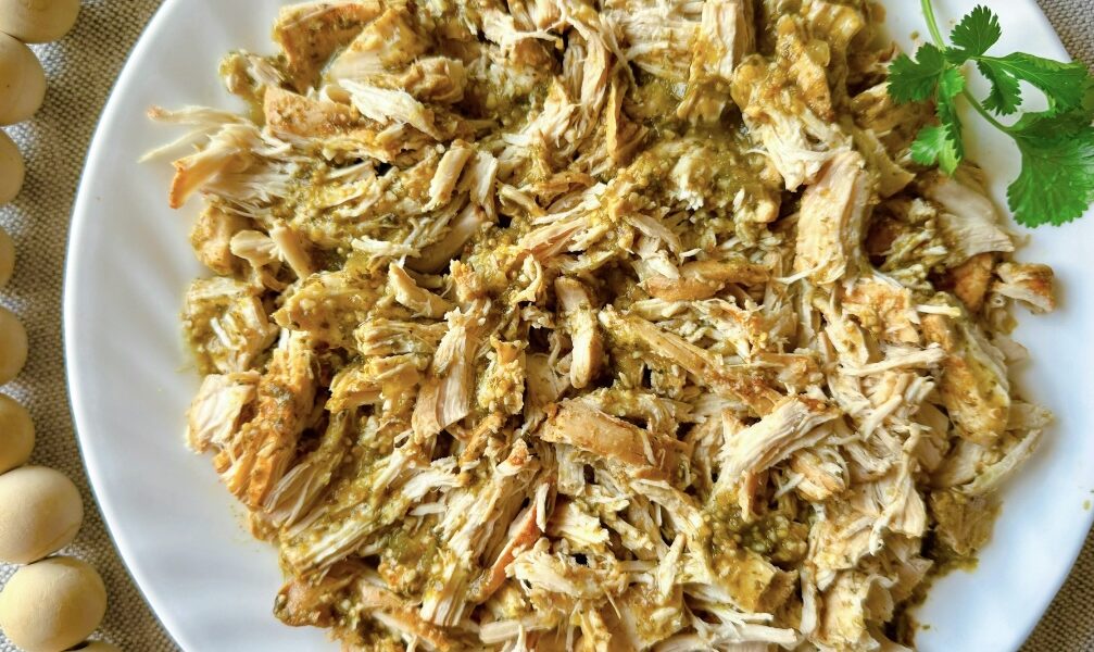 white plate on a table with a pile of shredded salsa verde chicken on it