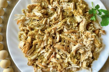 white plate on a table with a pile of shredded salsa verde chicken on it