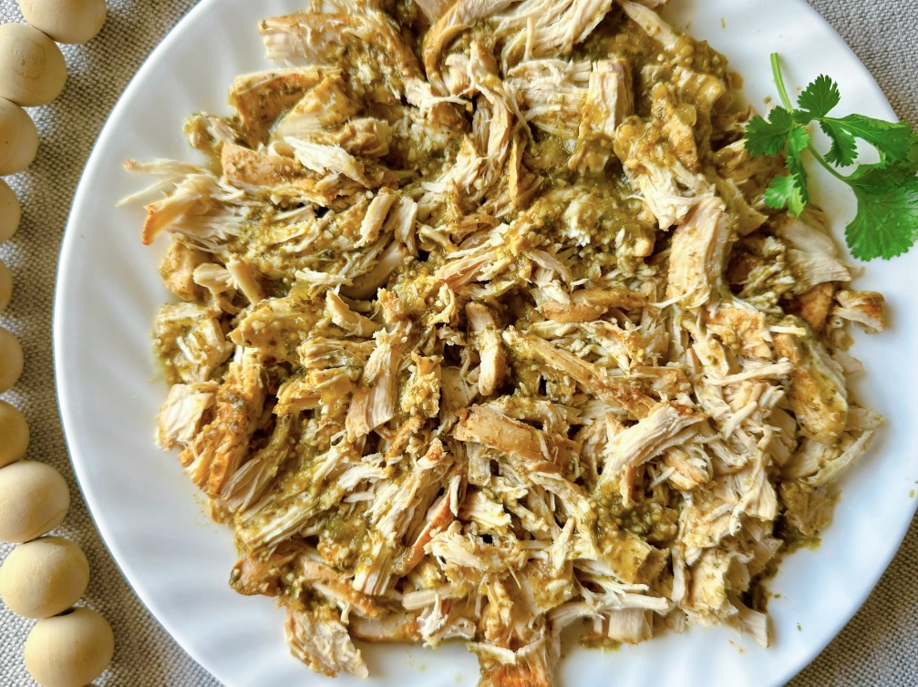 white plate on a table with a pile of shredded salsa verde chicken on it