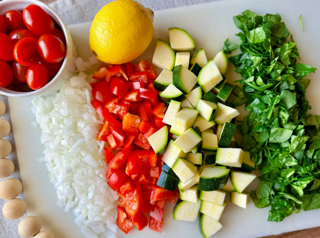 chopped onion, bell pepper, zucchini, spinach, cherry tomates and lemon flat lay on table