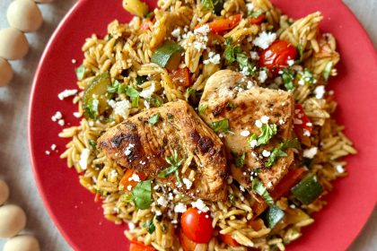 overhead shot of red plate with one pot mediterranean chicken and orzo on top garnished with feta cheese