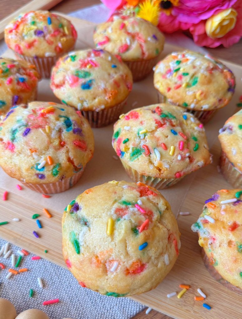 close up of funfetti muffins on a wooden tray and lots of colorful sprinkles laying around