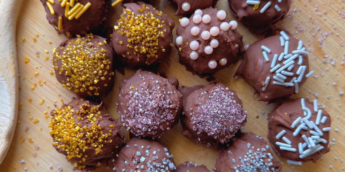 no bake chocolate cheesecake balls on wooden tray with colorful sprinkles