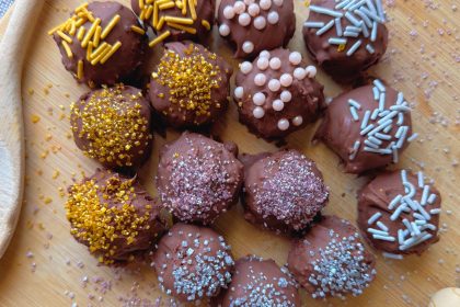 no bake chocolate cheesecake balls on wooden tray with colorful sprinkles