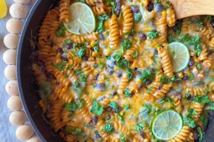 Overhead view of one pot Southwest pasta in a skillet with black beans, corn, tomatoes, lime slices and fresh cilantro.