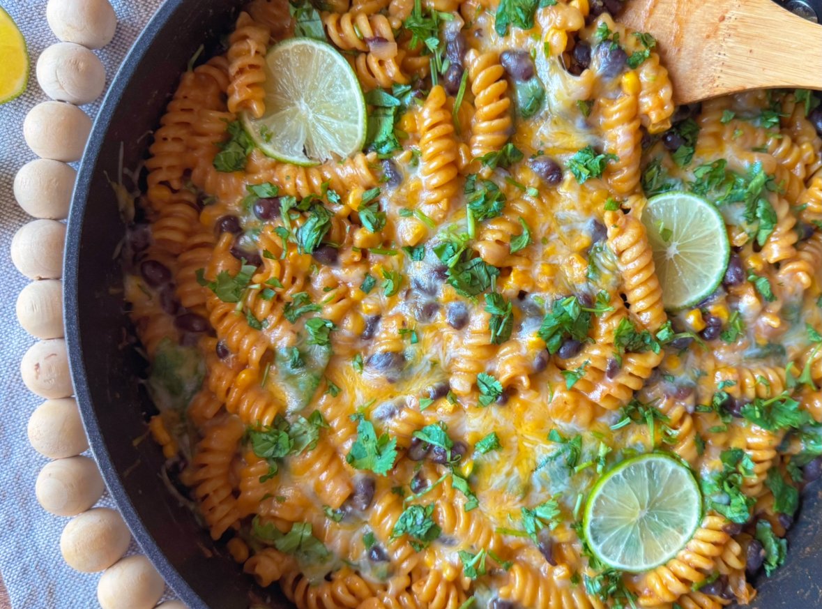 Overhead view of one pot Southwest pasta in a skillet with black beans, corn, tomatoes, lime slices and fresh cilantro.