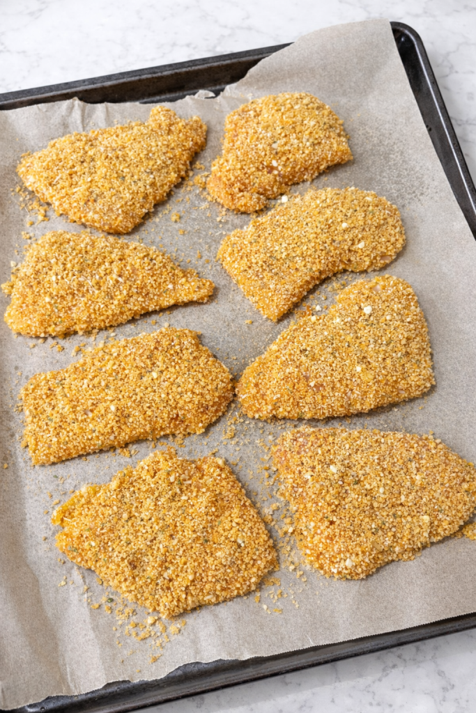 oven fried chicken on a baking sheet after dipped in breadcrumbs