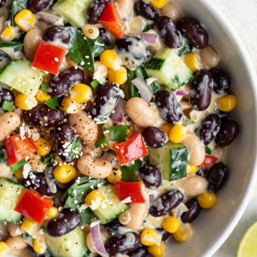 Creamy chipotle bean salad in a white bowl with black beans, white beans, corn, and fresh vegetables.