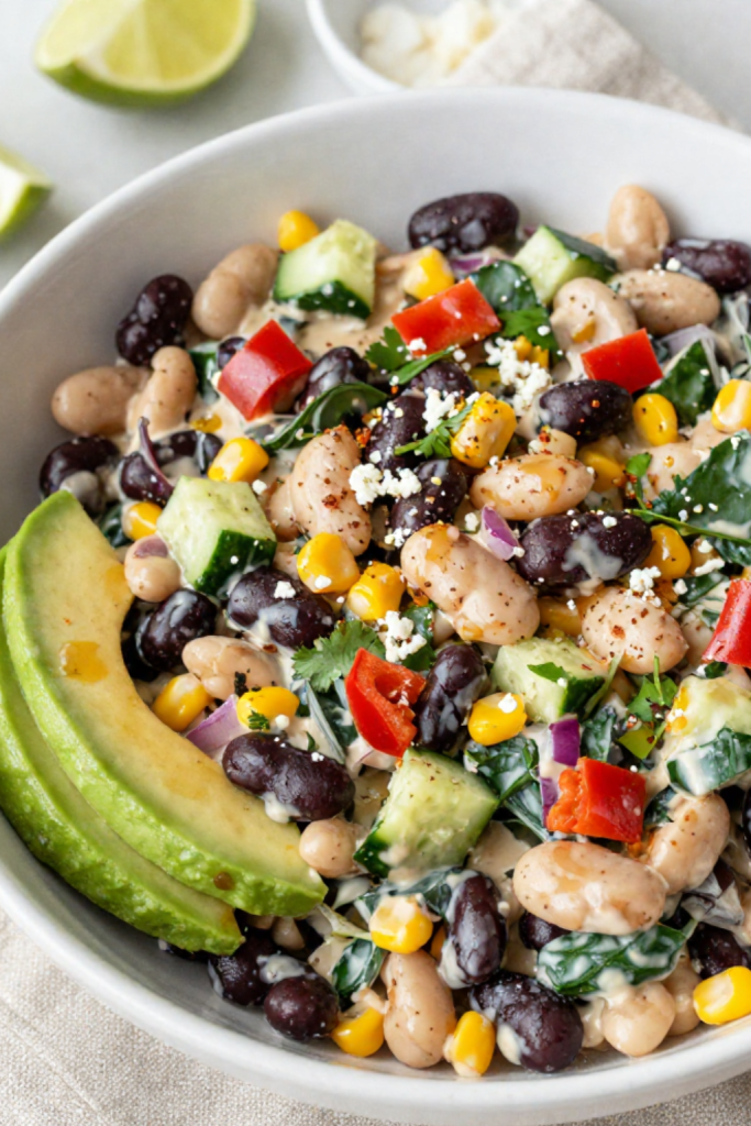Creamy high-protein bean salad in a bowl with black beans, white beans, corn, avocado and Greek yogurt dressing.