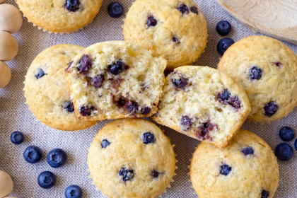 Lemon blueberry Greek yogurt protein muffins with one muffin cut in half showing fluffy texture and baked blueberries.