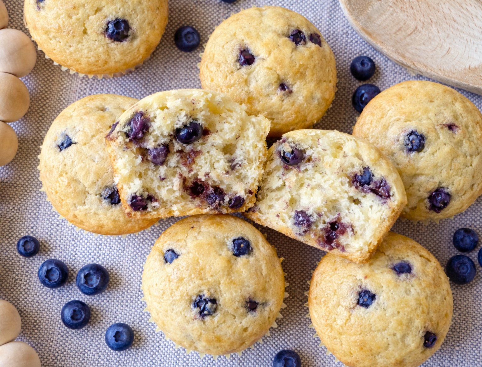 Lemon blueberry Greek yogurt protein muffins with one muffin cut in half showing fluffy texture and baked blueberries.