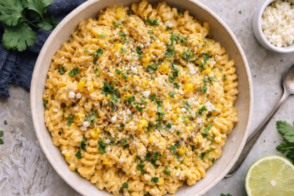 overhead shot of mexican street corn mac and cheese in a white bowl topped with cilantro and tajin