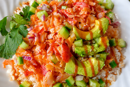 close up shot of a volcano roll sushi bowl with bright orange crab mixture on top and a drizzle of eel sauce