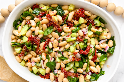 overhead shot of white bean salad in large serving bowl with cannellini beans, sun-dried tomatoes, spinach and cucumber