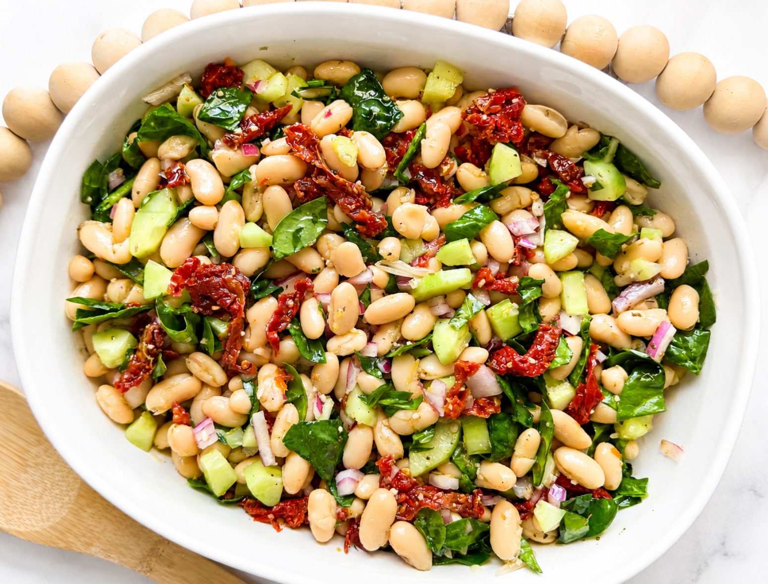 overhead shot of white bean salad in large serving bowl with cannellini beans, sun-dried tomatoes, spinach and cucumber