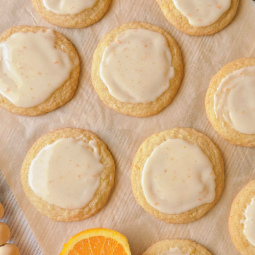 orange creamsicle cookies topped with glossy vanilla-orange icing. cookies are arranged flat on parchment paper