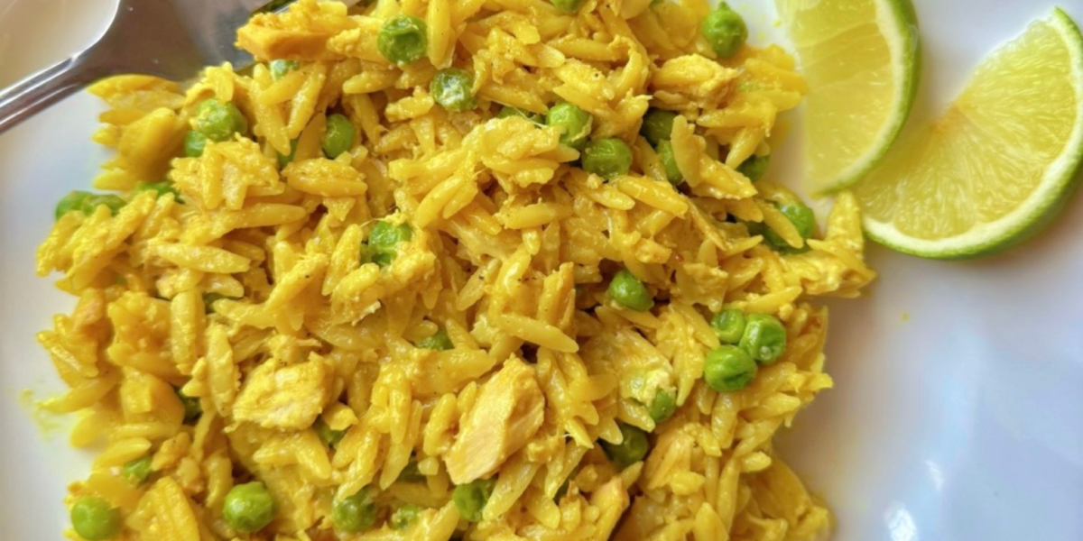 close up of curry orzo with tuna and peas on a white plate with lime wedge garnishes