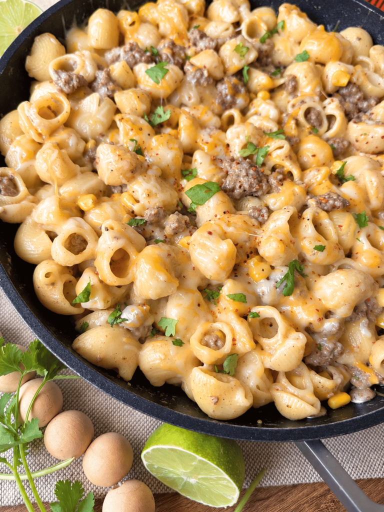 skillet with creamy chipotle lime beef pasta on a wooden table with cilantro and lime accents