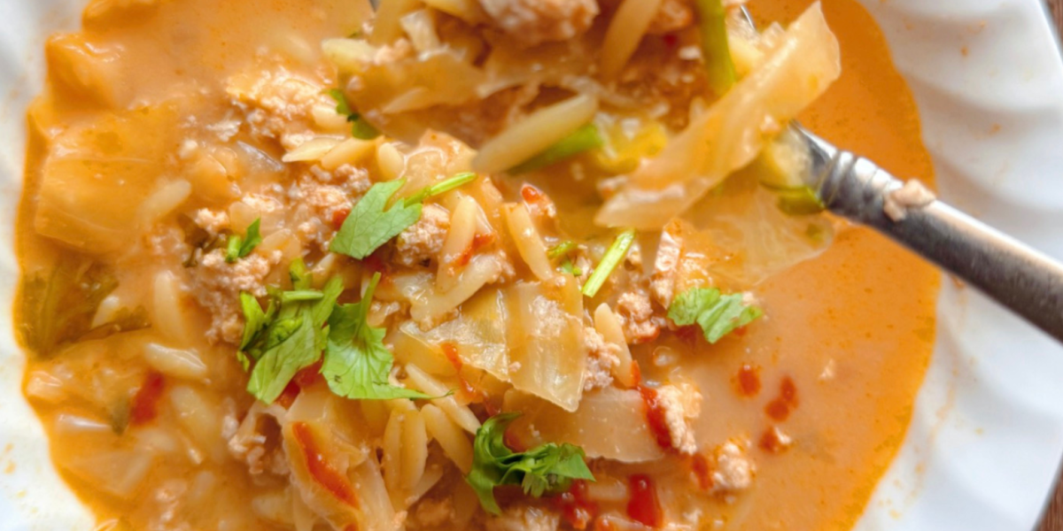 close up of spoon holding creamy curry egg roll soup with orzo drizzled with hot sauce and cilantro