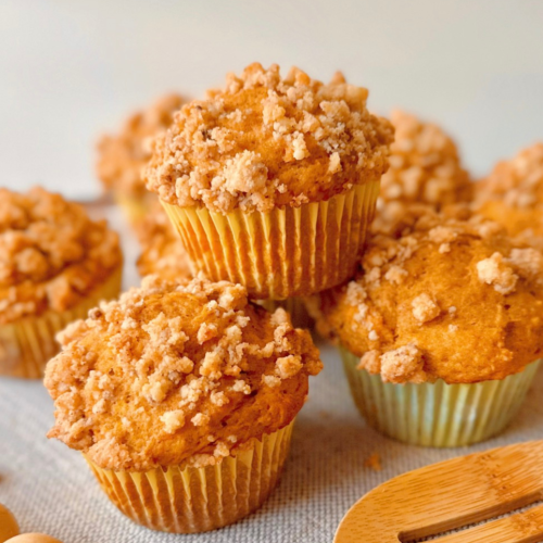 one pumpkin greek yogurt muffin with streusel on top of another muffin with streusel crumbs around them