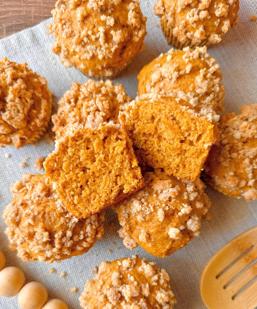 a greek yogurt pumpkin muffin split in half to show the soft inside. cinnamon streusel crumbs sprinkled around the muffins